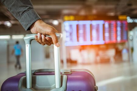 close up man hand touching baggage for check in at flight timetable in international airport.の写真素材