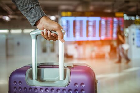 close up man hand touching baggage for check in at flight timetable in international airport.の写真素材