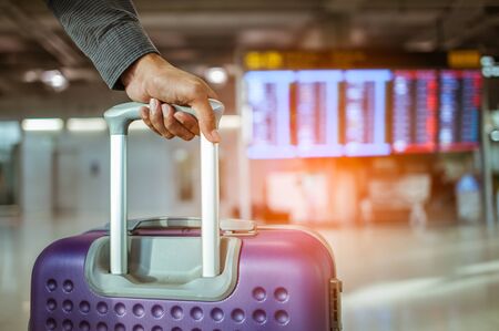 close up man hand touching baggage for check in at flight timetable in international airport.の写真素材