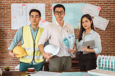 Team of architect are holding on blueprint and helmet working engineering or architecture project at office. Engineer, Engineering, Architecture, Blueprint, Planning, Occupation concept.の写真素材