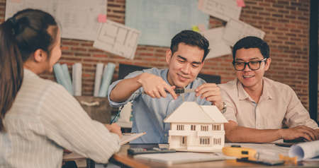 Male architect hands measuring and making model house with them team on the desk at sunset. Engineer, Engineering, Architecture, Design, Planning, Occupation concept.の写真素材