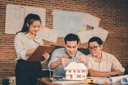 Male architect hands measuring and making model house with them team on the desk at sunset. Engineer, Engineering, Architecture, Design, Planning, Occupation concept.の写真素材