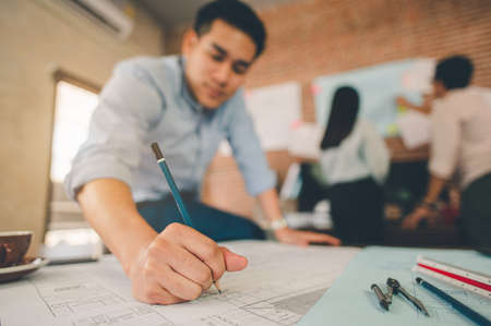 Close up of male architect hands writing model on the desk. Blurred behind team of engineer discussing of construction plan. Engineer, Engineering, Architecture, Design, Planning, Occupation concept.の写真素材