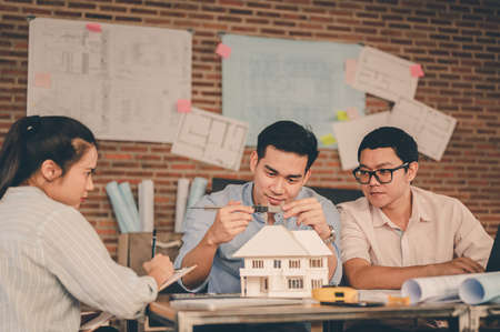 Male architect hands measuring and making model house with them team on the desk at sunset. Engineer, Engineering, Architecture, Design, Planning, Occupation concept.の写真素材