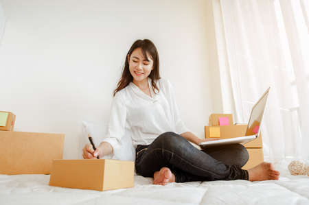 Young woman asian work from home talking with customers to sell products online and delivery for customer. Business owner, SME, shipping, work from home(WFH), freelance, Start up concept.の写真素材