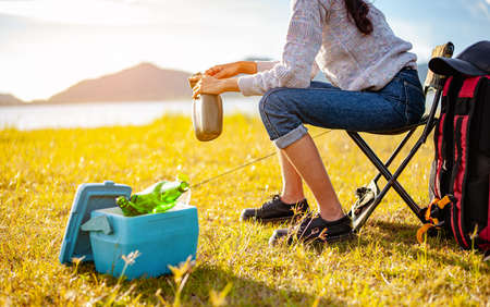 Female asian travelers are sitting and enjoying a drink after a set up outdoor tent in the forest path autumn season. Hiking, hiker, team, forest, camping , activity concept.の写真素材