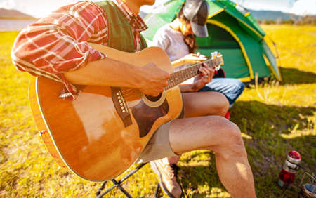 Team of asian climbers hiker are sitting and enjoying a drink after a set up outdoor tent playing music together in the forest path autumn season. Hiking, hiker, team, forest, camping, activity concept.の写真素材