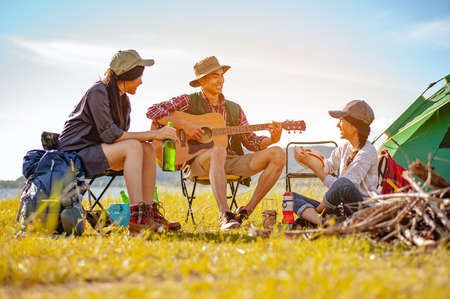 Team of asian climbers hiker are sitting and enjoying a drink after a set up outdoor tent playing music together in the forest path autumn season. Hiking, hiker, team, forest, camping, activity concept.の写真素材