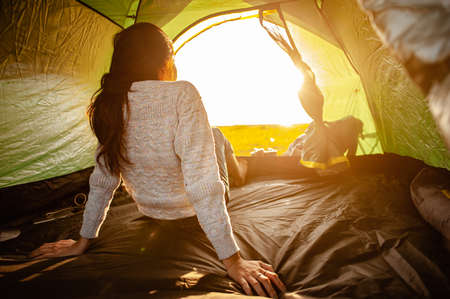 The woman asian who just woke up inside the tent was watching the sunrise in the morning as a holiday activity in the forest path autumn season. Hiking, hiker, alone, forest, camping, activity concept.の写真素材