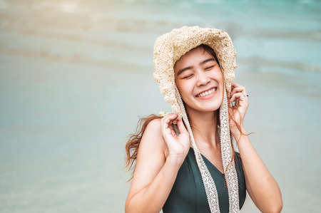 Happy asian women with holding hat stand to receive the wind and enjoy life on the beach vacation. beach, summer, liftstyle, positive mood, travel, relax concept.の写真素材
