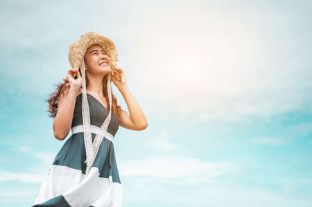 Happy asian women with holding hat stand to receive the wind and enjoy life on the beach vacation. beach, summer, liftstyle, positive mood, travel, relax concept.の写真素材