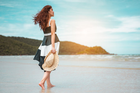 Happy asian women with holding hat stand to receive the wind and enjoy life on the beach vacation. beach, summer, liftstyle, positive mood, travel, relax concept.の写真素材