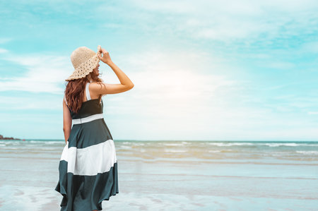 Happy asian women with holding hat stand to receive the wind and enjoy life on the beach vacation. beach, summer, liftstyle, positive mood, travel, relax concept.の写真素材
