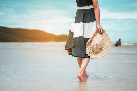 Happy asian women with holding hat stand to receive the wind and enjoy life on the beach vacation. beach, summer, liftstyle, positive mood, travel, relax concept.の写真素材