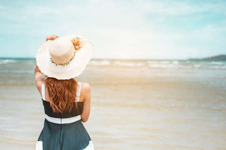 Happy asian women with holding hat stand to receive the wind and enjoy life on the beach vacation. beach, summer, liftstyle, positive mood, travel, relax concept.の写真素材