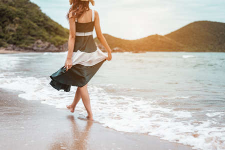 Happy asian women with holding hat walking barefoot to receive the wind and enjoy life on the beach vacation. beach, summer, liftstyle, positive mood, travel, relax concept.の写真素材