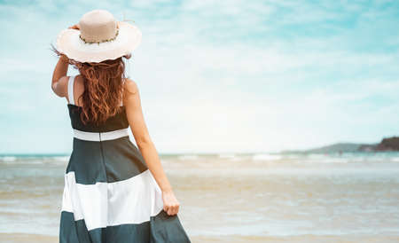 Happy asian women with holding hat stand to receive the wind and enjoy life on the beach vacation. beach, summer, liftstyle, positive mood, travel, relax concept.の写真素材