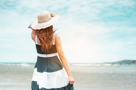 Happy asian women with holding hat stand to receive the wind and enjoy life on the beach vacation. beach, summer, liftstyle, positive mood, travel, relax concept.の写真素材