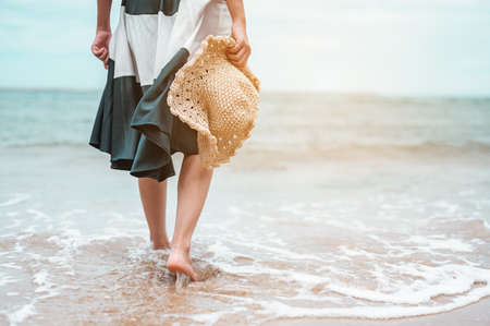 Happy asian women with holding hat walking barefoot to receive the wind and enjoy life on the beach vacation. beach, summer, liftstyle, positive mood, travel, relax concept.の写真素材