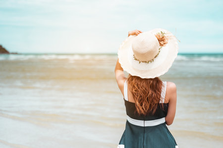 Happy asian women with holding hat stand to receive the wind and enjoy life on the beach vacation. beach, summer, liftstyle, positive mood, travel, relax concept.の写真素材