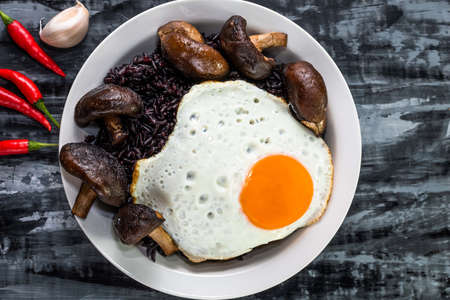 Black rice in bowl dish with mushroom have fried egg garlic chili isolated on grey background close up, top view, healthy food and drink concept.の写真素材