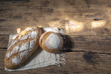 baguette and round bread isolated on wood background, gold rustic crusty bun have sun highlight, top view, food and drink concept.の写真素材