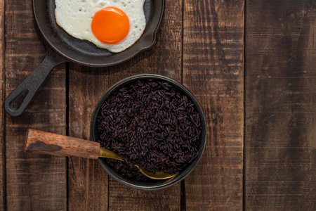 Black rice in bowl dish have fried egg in pan isolated on wood background close up, top view, healthy food and drink concept.の写真素材