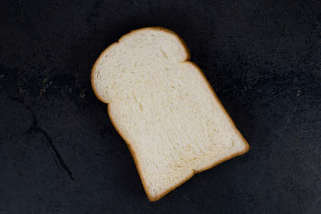 White bread slice isolated on black stone background closeup, top view, copy space, breakfast food...
