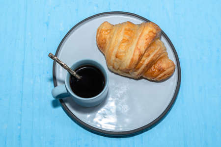 Espresso coffee and croissant in plate on isolated blue table background close up, top view,...