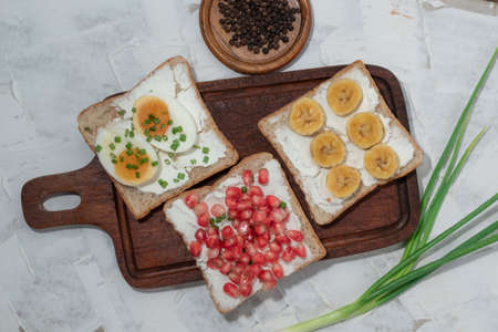 Bread slice add cream cheese spread with pomegranate boiled egg banana in cutting board isolated on white wood background close up, top view, breakfast food concept.の写真素材