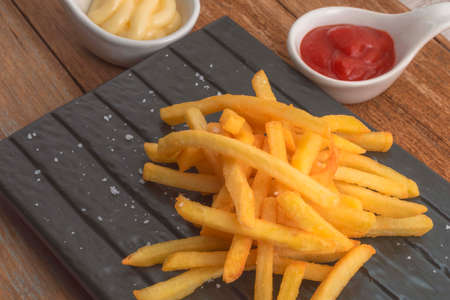 French fries in slate has mayonnaise and tomato sauce on wood background unhealthy food concept.