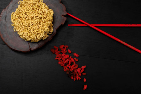 Yellow instant noodle on black wood background has red chopsticks wolfberry, top view, Asian food concept.の写真素材