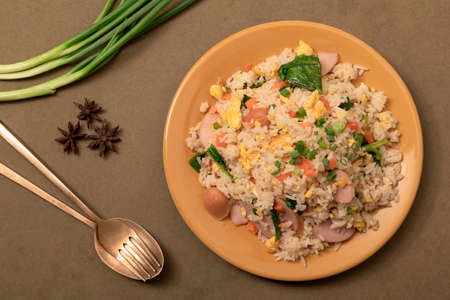 Fried rice with sausage egg carrot in yellow plate has spoon isolated on brown background close up, top view, Asian food concept.の写真素材