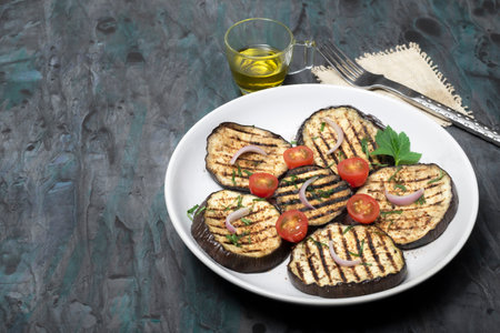 Grilled eggplants in plate has fork on isolated on black wood background close up, top view, healthy food concept.の写真素材