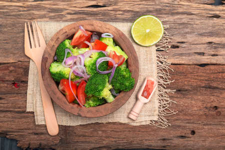 Broccoli salad has tomato in bowl isolated on wood background close up, top view, healthy vegetable food concept.の写真素材