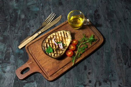 Grilled eggplants in cutting board has fork and olive oil garlic isolated on black background close up, top view, healthy food concept.の写真素材