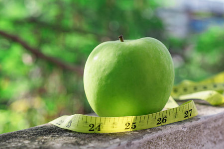 Measure tape and green apple on stone background close up, healthy food concept.の写真素材