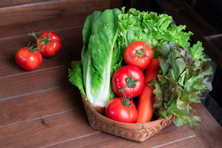 Red lettuce and romaine tomato carrot in basket on wood table, top view, copy space, healthy food concept.の写真素材