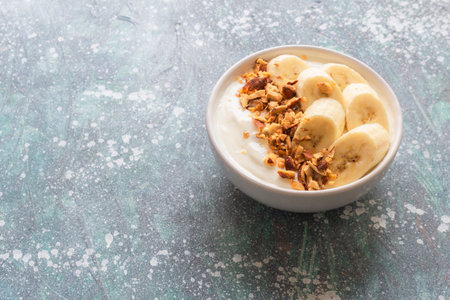 Yogurt in bowl has banana almonds on blue wood background, top view, healthy food concept.の写真素材
