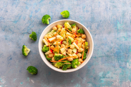 Broccoli salad add apple chickpeas in white bowl isolated on blue wood background close up, top view, healthy food concept.の写真素材