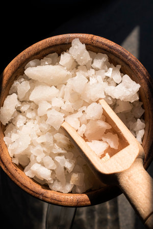 Sea salt crystals in bowl isolated on black stone background close up, top view, copy space, food and drink concept.の写真素材