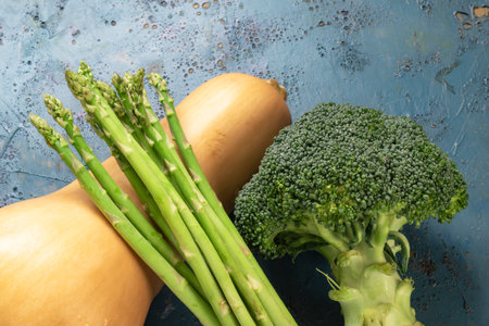 Fresh broccoli asparagus butternut squash vegetables on blue wood background copy space, top view, healthy food concept.の写真素材