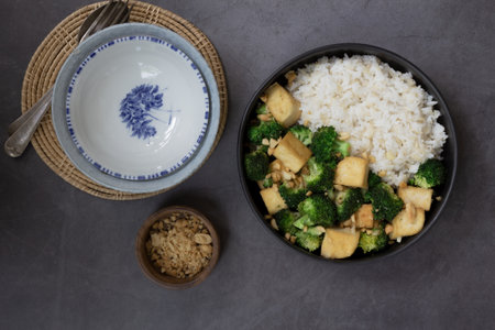 Stir fried broccoli tofu peanuts has brown rice in black bowl on loft background, top view, vegan healthy food conceptの写真素材