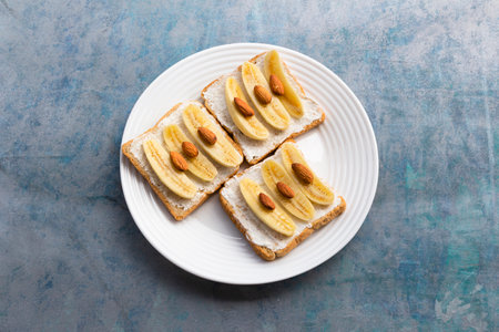 Sandwich open has banana cream cheese almonds on wood background, top view, copy space, breakfast...