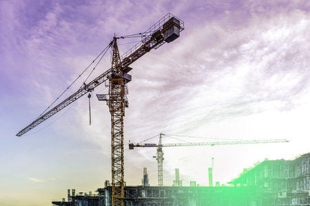 Building construction site with flare light on sunset sky cloud, Engineering work on construction with silhouetted sky at sunset, Factory site with yellow light against blue sky, Industrial growingの写真素材
