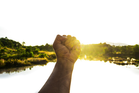Hands clenched fist, Fist grip, Frighting sign by hand, Concentrate to your goal, Flare light from sunrise with cold air in winter, Symbols of hope, Man hand hold the index finger and middle fingerの写真素材