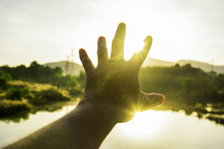 Use hand to touch the sun light in the morning, Pick up the sun by hand, Close the sun in your hand, Yellow light with cold air in winter, Flare from sunrise, Symbols of hopeの写真素材