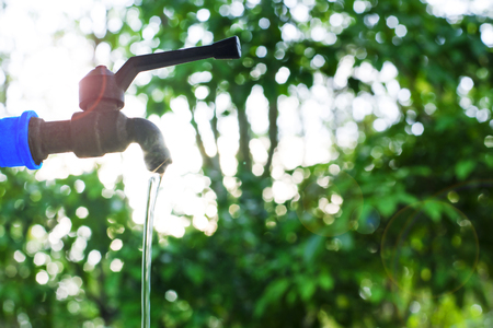 Water valve on green nature background, Close up tap valve with blur background of green tree, Water drop from steel faucet to waste, Water saving concept, Energy conservative background, Flare lightの写真素材