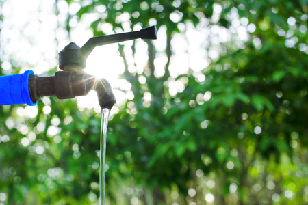 Water valve on green nature background, Close up tap valve with blur background of green tree, Water drop from steel faucet to waste, Water saving concept, Energy conservative background, Flare lightの写真素材