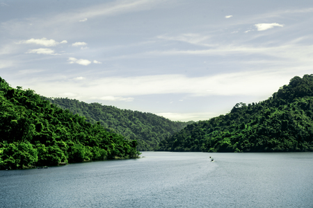 Beautiful landscape view of green mountain beside river on bright sky clouds, Water storage dam, Green tree nature mountain on riversideの写真素材